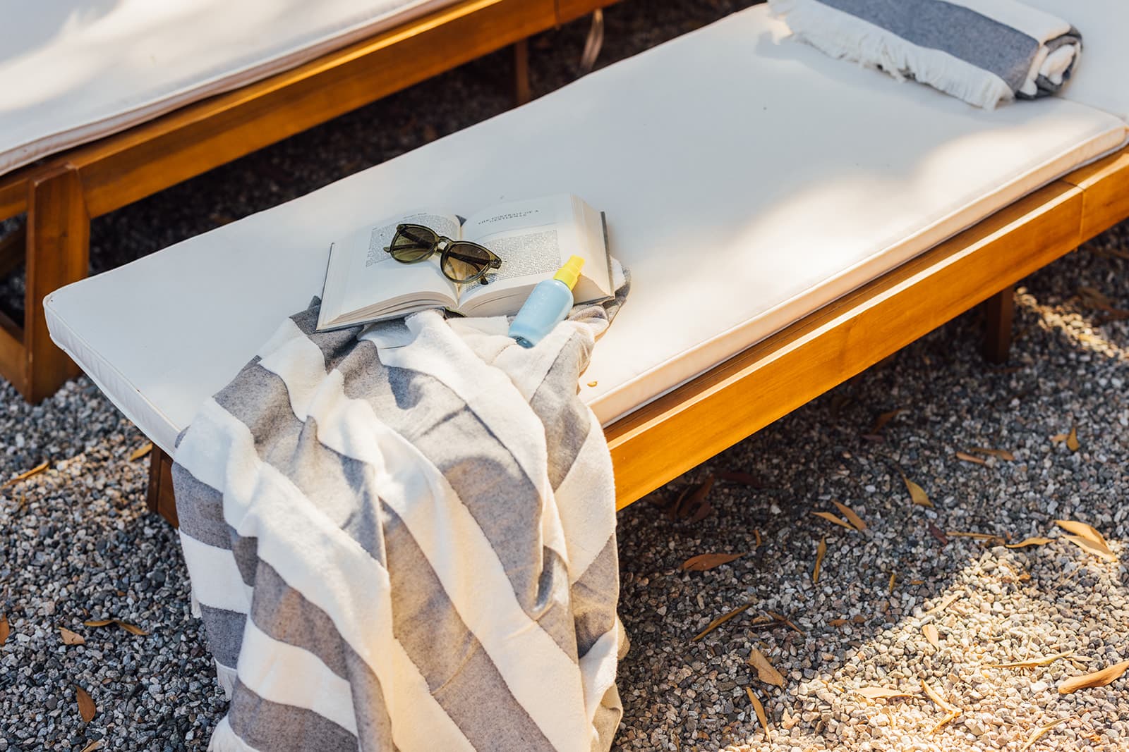 An open book and sunglasses on a wooden sun lounger, a striped towel draped over the edge in the afternoon garden