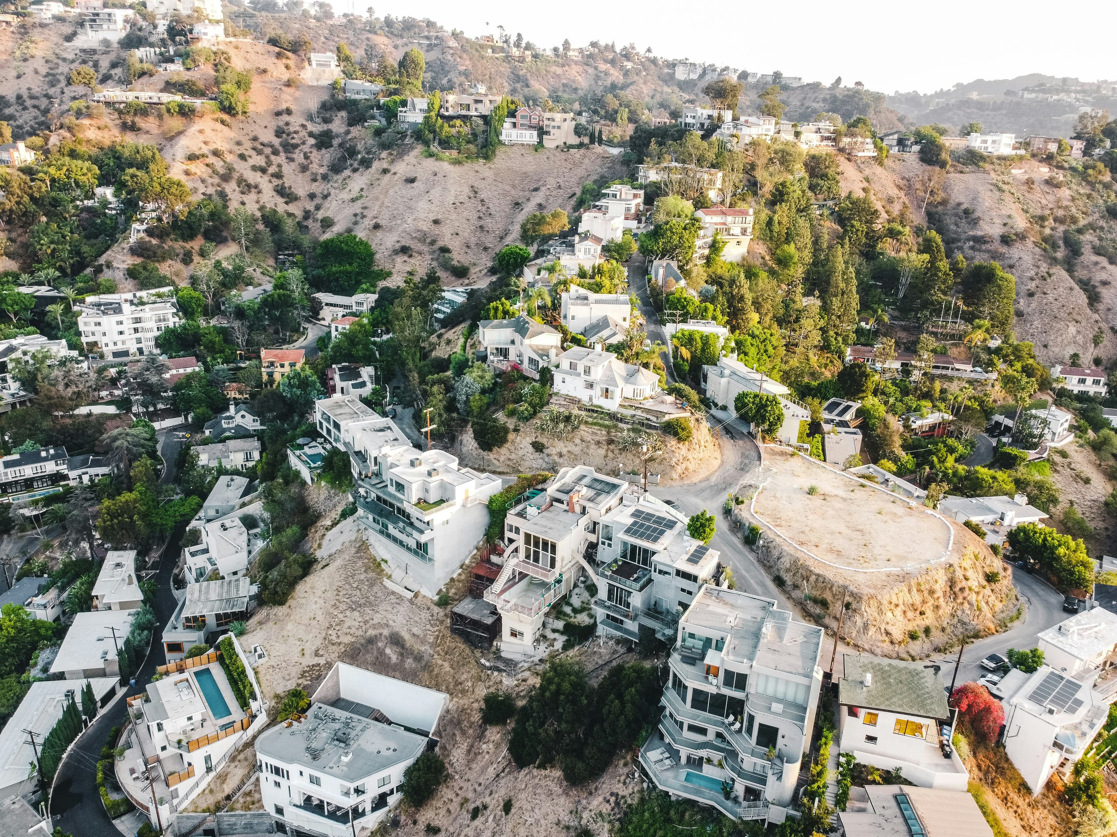 Aerial view of white hillside houses stacked down a Laurel Canyon ridge, switchback roads folding between them